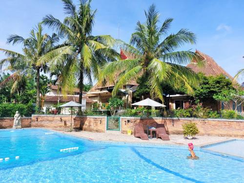 a swimming pool in front of a resort with palm trees at Hotel Deli River and Restaurant Omlandia in Medan