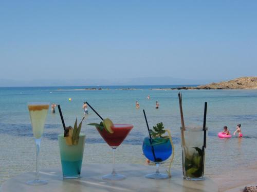 a table with drinks on the beach with people in the water at Antonios Village Hotel & Apartments in Arkoudi