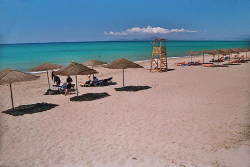 a beach with umbrellas and people sitting on the sand at Antonios Village Hotel & Apartments in Arkoudi
