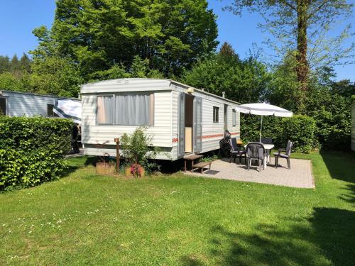 a white caravan in a yard with a table and an umbrella at Ferienpark Eifellux in Körperich