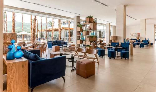 eine Lobby mit blauen Stühlen, Tischen und Fenstern in der Unterkunft Gomeh by Isrotel Design in Tiberias