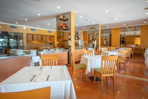 a restaurant with white tables and chairs and a kitchen at Hotel da Aldeia - Adults Only in Albufeira