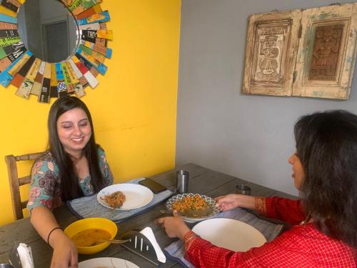 dos mujeres sentadas en una mesa comiendo comida en Bed & Chai Guesthouse, en Nueva Delhi