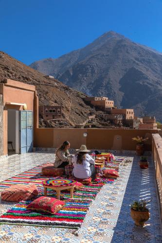 two people sitting on a rug with a mountain in the background at Amazigh Family Riad in Imlil