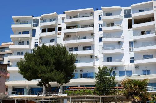 a white apartment building with a tree in front of it at Oceanic Overview Suites in Sarandë
