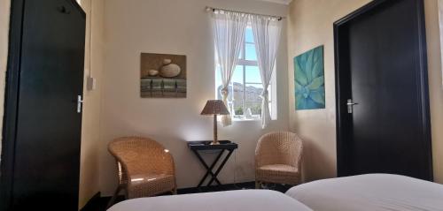a bedroom with a bed and two chairs and a window at Cozy room in the Heart of Simon's Town in Cape Town
