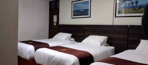 three beds in a hotel room with white and brown sheets at HOSTAL CORAL in Ilo