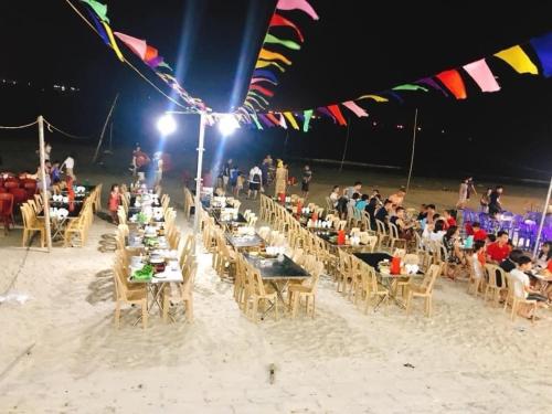 a group of people sitting at tables on the beach at night at Minh Huy Hotel in Quang Ninh