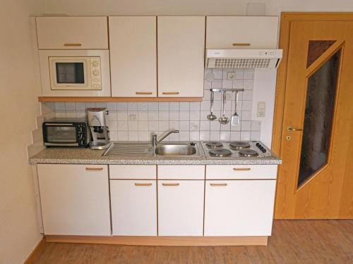 una pequeña cocina con armarios blancos y fregadero en Apartment Almrausch by Interhome, en Fendels