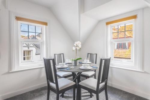 a dining room with a table and chairs and two windows at Coast View Luxury Apartment in Lyme Regis