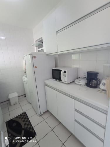 a white kitchen with a microwave and a refrigerator at Village Hospedagens in Natal