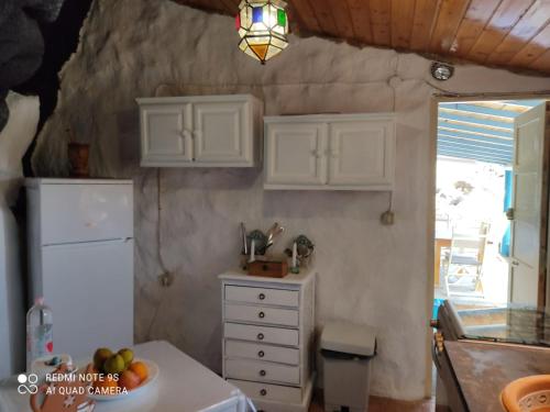een keuken met witte kasten en een tafel met een fruitschaal bij casa cueva el Pozo las Calcosas in Pozo de las Calcosas