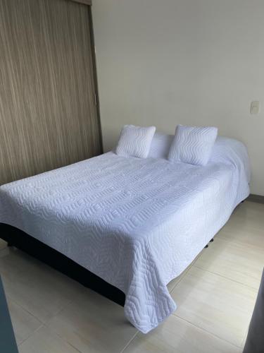 un letto con lenzuola e cuscini bianchi in una stanza di Apartasuite 01 a Pereira