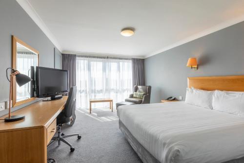 a hotel room with a bed and a desk with a television at Holiday Inn Basildon by IHG in Basildon