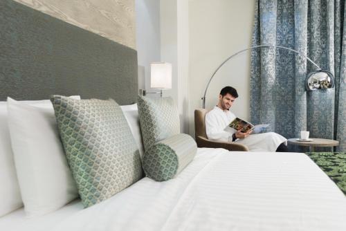 a man sitting in a chair reading a book in a bedroom at Centara Muscat Hotel Oman in Muscat