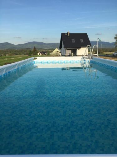 a pool of blue water with a house in the background at Osada Zdrojowa u Martyny in Długopole Dolne
