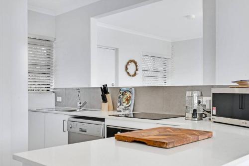 a white kitchen with a wooden cutting board on a counter at Coastal Chic Apartment - Mooloolaba and Alex in Alexandra Headland