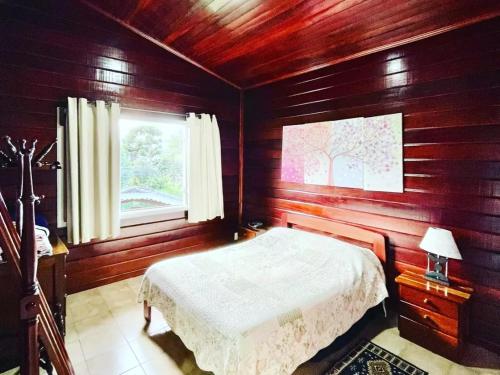 a bedroom with wooden walls and a bed with a window at Chalé Manacá House in Campos do Jordão