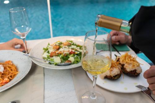 a person pouring white wine into a wine glass at Mossa Well Being Hotel - Heated pool in Kato Daratso