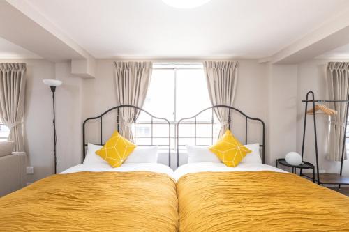 1 Schlafzimmer mit 2 Betten mit gelber Bettwäsche und einem Fenster in der Unterkunft アリタ日本橋西3F in Osaka