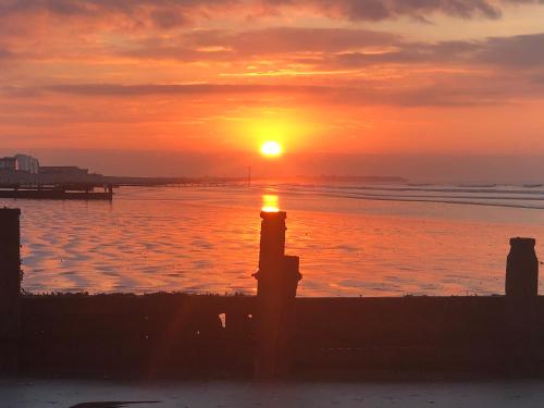 a sunset over the ocean with a lighthouse at The Shack in East Wittering