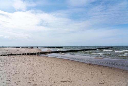a sandy beach with a pier in the ocean at Rowy Apartamenty Jantar 75 m od plaży in Rowy