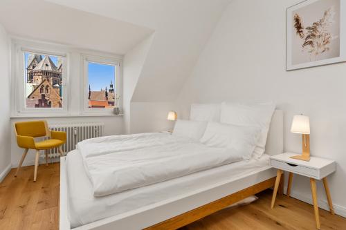 a white bed in a room with a chair and two windows at City-Apartment⎪Domblick⎪Marktplatz in Bremen
