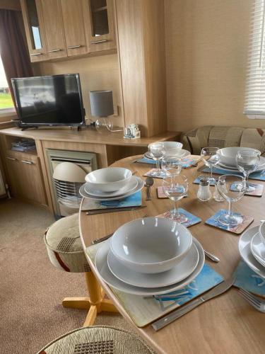 a wooden table with plates and wine glasses on it at Comfy 2 bed holiday caravan in Whitstable