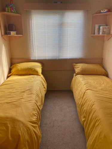 two beds in a bedroom with yellow sheets and a window at Comfy 2 bed holiday caravan in Whitstable