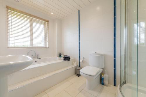 a white bathroom with a tub and a toilet and a sink at Alton Villa, Sleeps 10, Great for Families, Undercover Hotub & Games Room in Newmilns