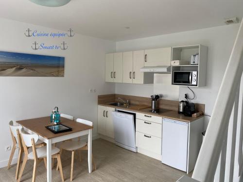 a kitchen with white cabinets and a table with chairs at Duplex moderne à 700m de la plage Parking & WiFi in Fort-Mahon-Plage