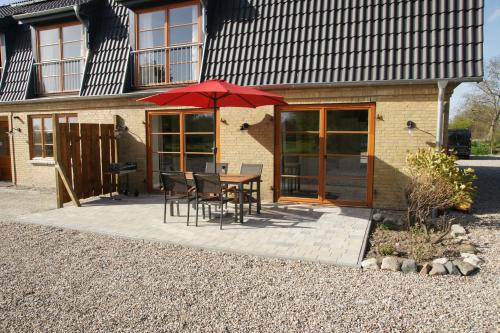 eine Terrasse mit einem Tisch, Stühlen und einem roten Regenschirm in der Unterkunft Hof Ruemland Ferienwohnungen in Hollingstedt
