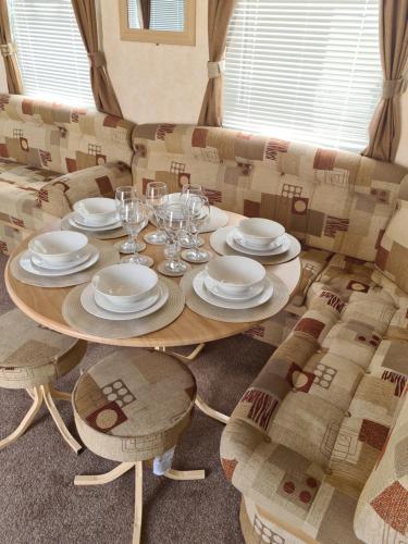 チャペル・セント・レオナルズにあるSuperb 8 Berth Caravan, Golden Anchor Parkのソファの上に皿とグラスをかけたテーブル