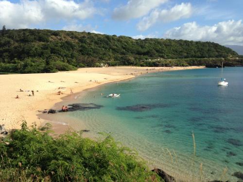 a beach with people and a boat in the water at Waimea Bay Garden Bunglaow in Haleiwa