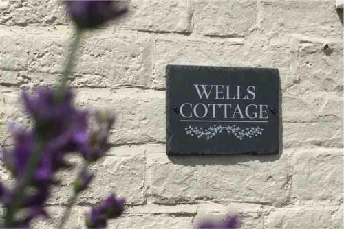 um sinal numa parede de tijolos com flores roxas em Wells Cottage em Malvern Wells