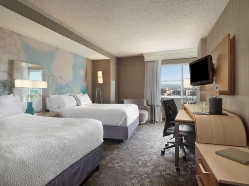 a hotel room with two beds and a desk at Sonesta Emeryville San Francisco Bay Bridge in Emeryville