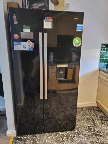 a black refrigerator in a kitchen next to a wall at Lovely 2 Bed Flat/Apt in East London- Nice Estate. in Dagenham
