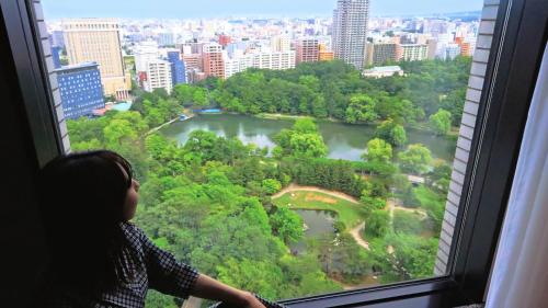 Una mujer mirando por una ventana en un parque en Premier Hotel Nakajima Park Sapporo, en Sapporo