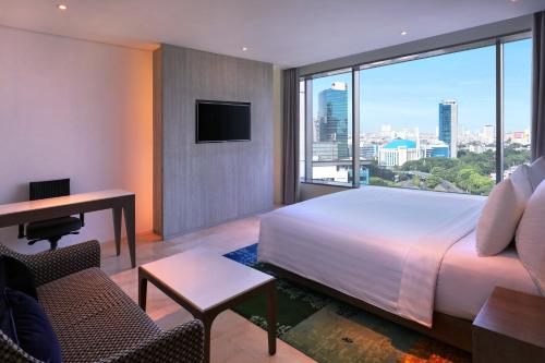 a bedroom with a bed and a desk and a large window at Grand Mercure Jakarta Kemayoran in Jakarta