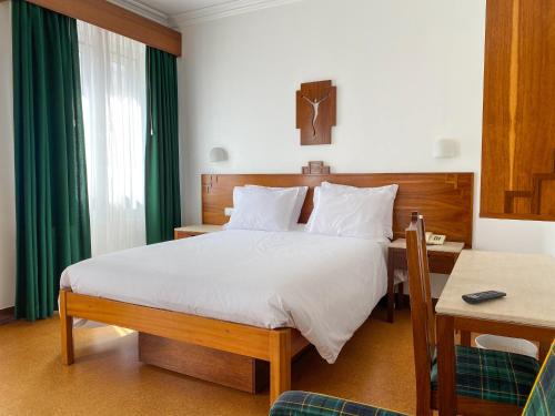 a bedroom with a large bed with a desk and a green curtain at Flag Hotel Fatima Casa Das Irmas Dominicanas in Fátima