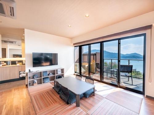 a living room with a table and a large window at LiVEMAX RESORT Miyahama Ocean View in Hatsukaichi