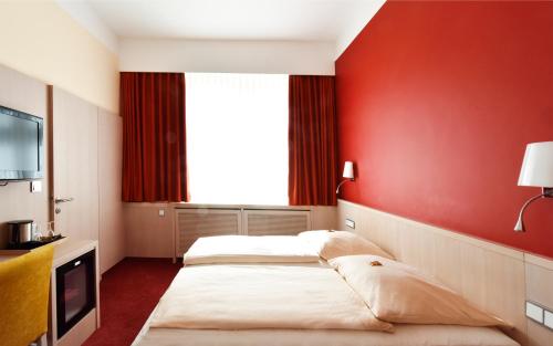 two beds in a room with a red wall at Hotel ADRIA München in Munich