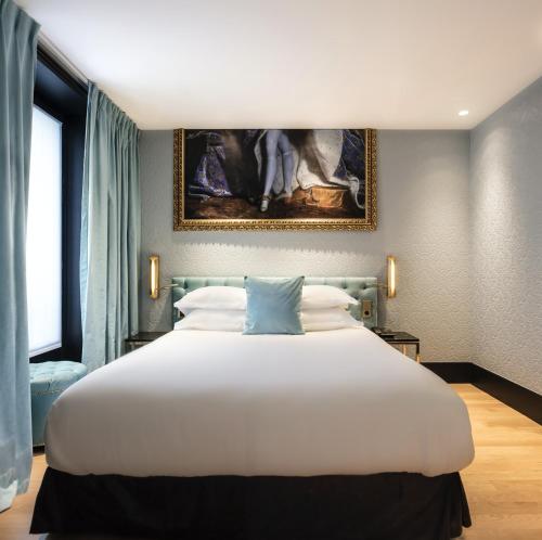 a bedroom with a large white bed with a painting on the wall at Eiffel Petit Louvre in Paris
