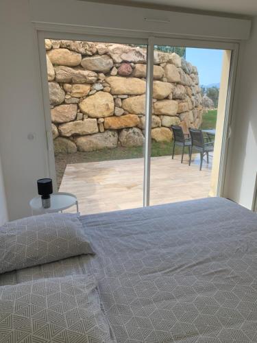 um quarto com uma cama e uma parede de pedra em CORSE HOLISTIKA - Rez-de-jardin avec vue mer exceptionnelle et piscine magnifique em Pietrosella