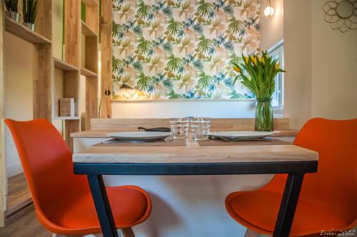 einem Esstisch mit orangefarbenen Stühlen und einer Vase aus Blumen in der Unterkunft Le T.Wood in La Gorgue