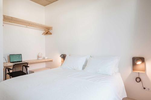 a bedroom with a white bed and a desk with a computer at B.Hostel in Comporta