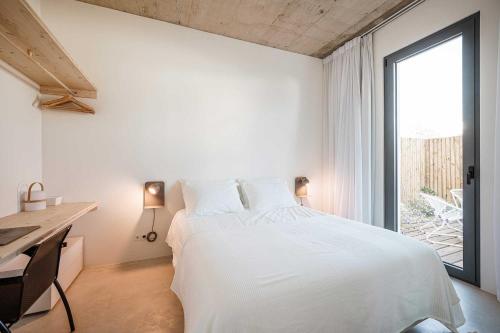 a bedroom with a white bed and a desk and a window at B.Hostel in Comporta