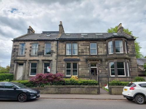 a stone house with two cars parked in front of it at Edinburgh House Hotel in Edinburgh