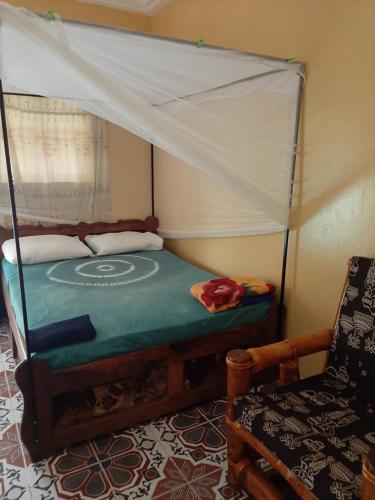 a bed with a canopy in a room with a chair at Franco Inn Guesthouse in Tanji