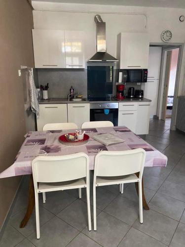a kitchen with a table with white chairs and a purple table cloth at Les Palmiers in Millau
